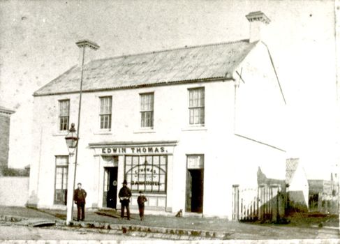 Two story hotel with multi panel window two men and a boy posing on footpath