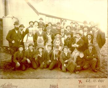 Black and white photograph of a group of men and boys posed outside the buildings of the rabbit factory