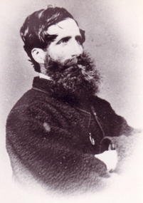 Profile of gentleman with dark hair and curly beard. he has his arms crossed