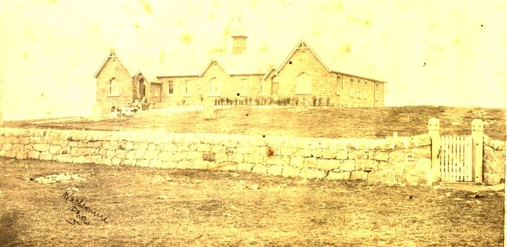 Consolidated school on hill with pupils outside and stone fence 