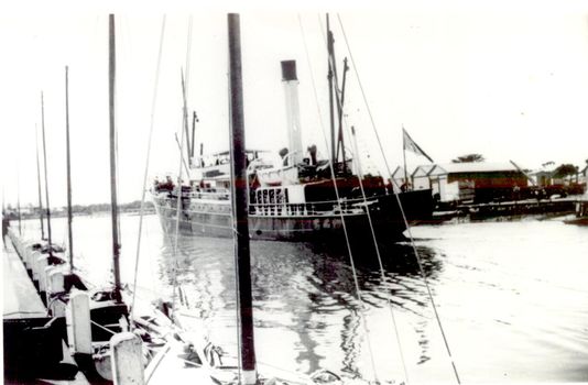 Ship coming into port heading for the turning basin, Shed on Eastern side of the river and couta boats tied up on the western side