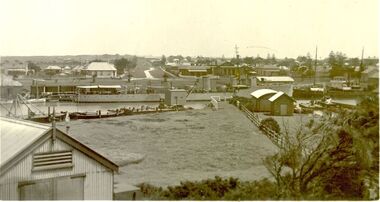 Large naval ship berthed at Port Fairy wharf with dredges and lifeboat sheds in foreground