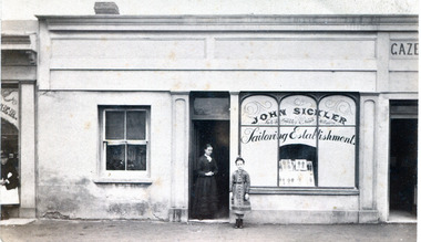 shop front with arched windows on right hand side and a female and a young girl standing in the doorway