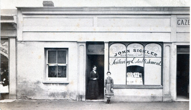shop front with arched windows on right hand side and a female and a young girl standing in the doorway