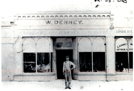 male standing on footpath outside shop with two arched windows either side of shop door