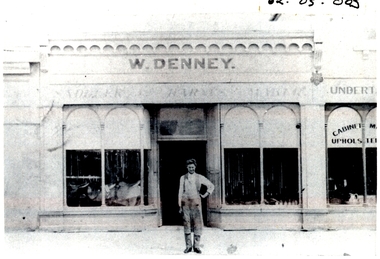 male standing on footpath outside shop with two arched windows either side of shop door