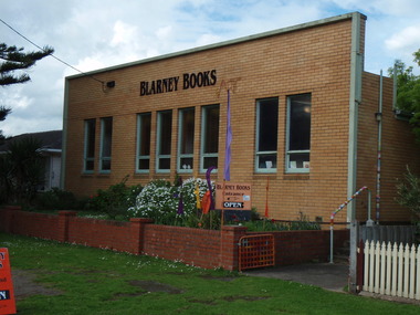 Brick fronted building set back from street with small garden in front entrance to side