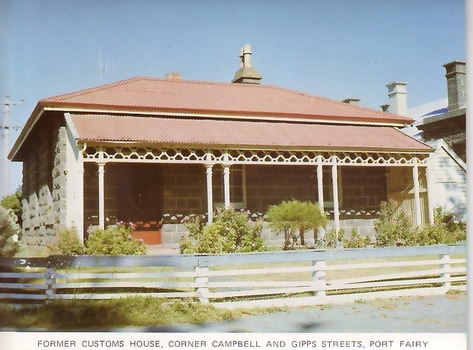 Blue stone cottage with verandah has iron posts and timber rail fence shed to right