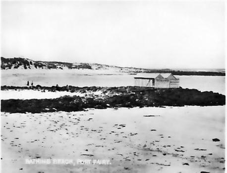 Beach with rock reefs across sand and wooden bathing boxes Dunes in background