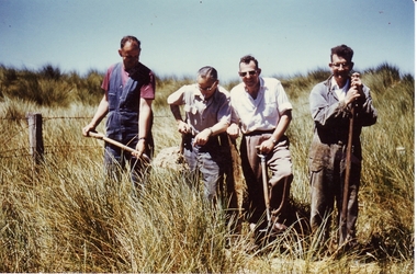 4 males working with spades inside a barbed wire fence with a large boulder in the background
