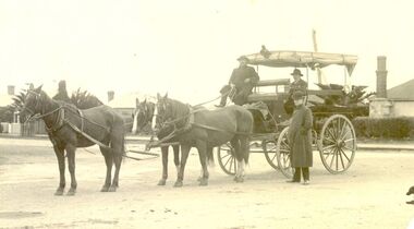 Horse drawn dray with seats for passengers around sides and drop down canvas blinds.3 horses harnessed and 3 males observing