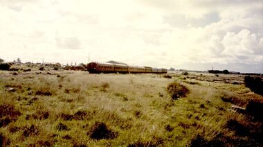 Wide expanse of rough grass with train moving into the distance. Glaxo’s chimney can be seen in the distance.