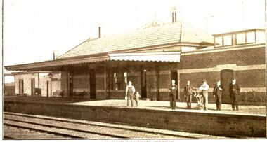 Koroit Railway station built with red bricks and 2 bands of cream one over the door ways- with 6 males and a child on the platform