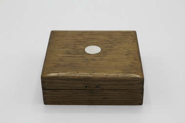Closed light coloured wooden box with escutcheon on lid