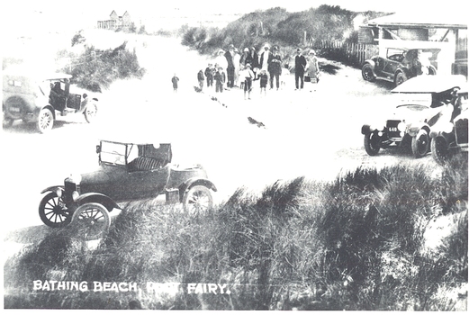 A black and white postcard  of The South Beach at the pavilion with cars In the foreground a group of people standing near the pavilion