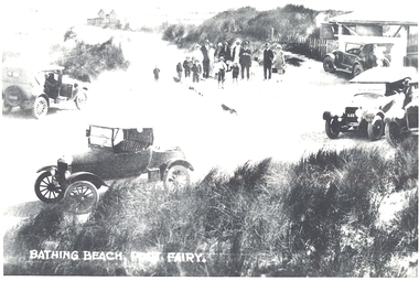 A black and white postcard  of The South Beach at the pavilion with cars In the foreground a group of people standing near the pavilion
