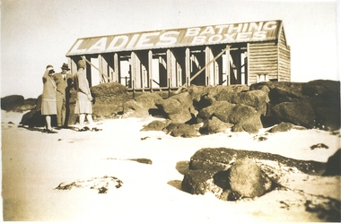 Ladies bathing boxes on stone reef with two women and a man standing in front