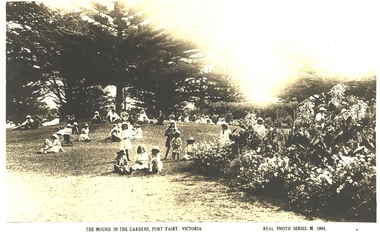 Several groups of adults and children sitting on the mound in the gardens
