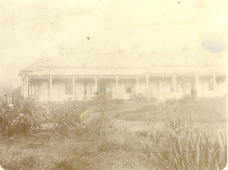 Large garden with curving path in front of large weatherboard house with verandah 
