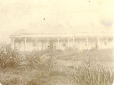 Large garden with curving path in front of large weatherboard house with verandah 