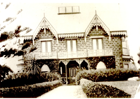Black and white photograph of the front of the two story house with short hedges lining the path to the front door