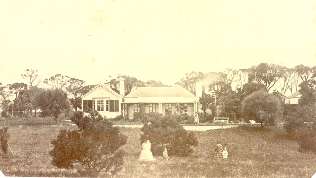House with a later edition added to the left all the buildings have large windows and patio doors. Two women and three children in the foregroundp