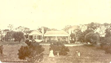 House with a later edition added to the left all the buildings have large windows and patio doors. Two women and three children in the foregroundp