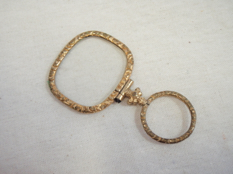 A gold coloured decorative eye glass with a finger holder 