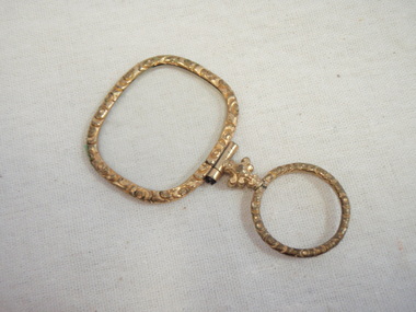 A gold coloured decorative eye glass with a finger holder 