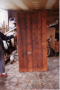 Wooden door supported by unknown person. Bicycles in background