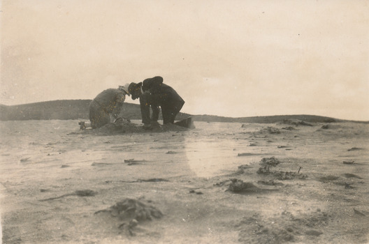 Two people kneeling in the sand digging up sand worms for fishing