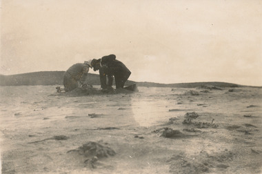Two people kneeling in the sand digging up sand worms for fishing