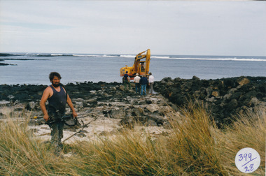 Male with brush cutter , large mechanical digger in background