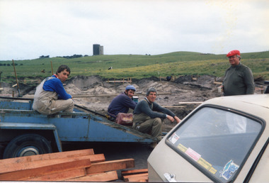 Three  males sitting on trailer talking to  another male standing 