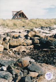 Rocks and drain on beach with A framed house being built in background