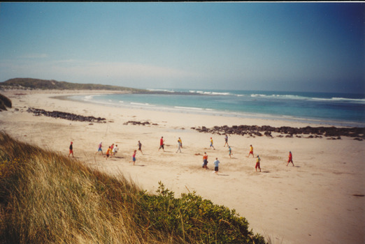 Coloured photograph of a wide sweep of sand and rock reef with a many people in the middle ground