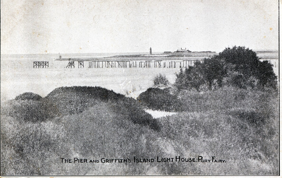 Black and white photograph of the remnants of the Campbell Street Pier with the lighthouse and its buildings in the background