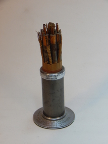 Metal cylinder with round base containing various wire cables wrapped in paper in tight bundle. 