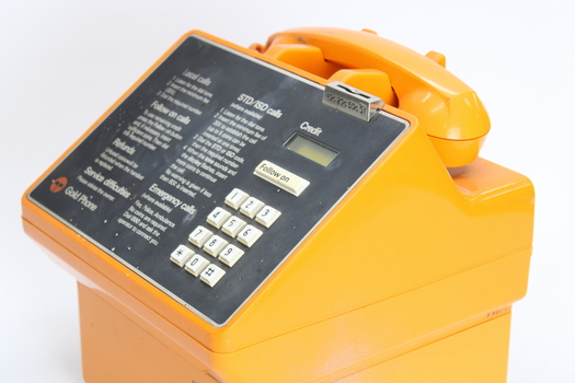 Orange plastic bodied public payphone with grey face and white dial buttons.