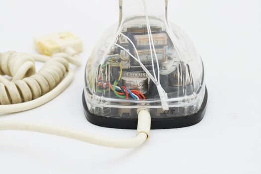Clear plastic telephone with dial underneath long stemmed handle; colourful electrical wires visible within.