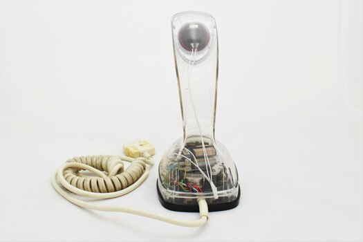 Clear plastic telephone with dial underneath long stemmed handle; colourful electrical wires visible within.