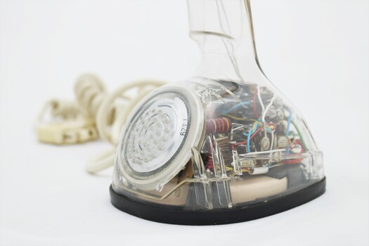 Clear plastic telephone with dial underneath long stemmed handle; colourful electrical wires visible within.