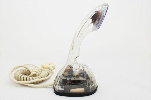 Clear plastic telephone with dial underneath long stemmed handle; colourful electrical wires visible within.