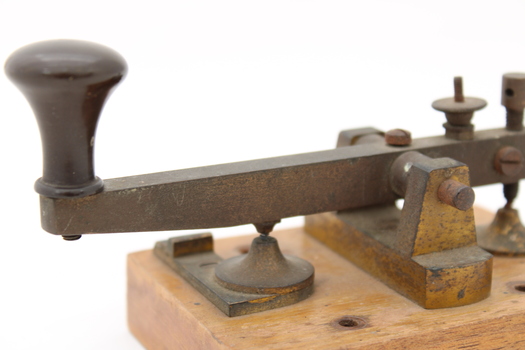 Metal device mounted on block of wood with handle that moves up and down via a spring.