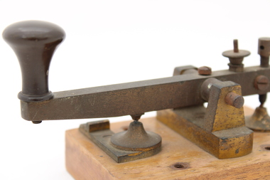 Metal device mounted on block of wood with handle that moves up and down via a spring.