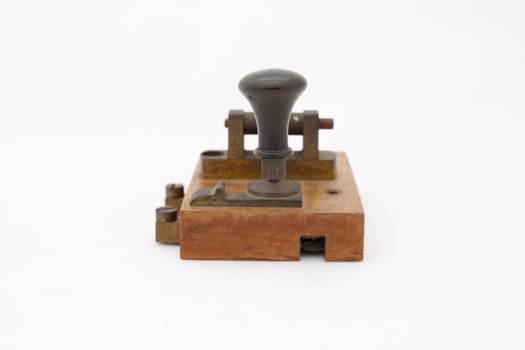Metal device mounted on block of wood with handle that moves up and down via a spring.