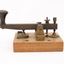 Metal device mounted on block of wood with handle that moves up and down via a spring.