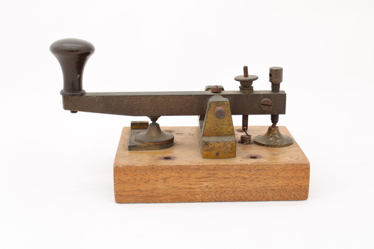 Metal device mounted on block of wood with handle that moves up and down via a spring.