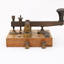Metal device mounted on block of wood with handle that moves up and down via a spring.