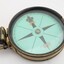 Gold coloured metal compass case with engraved lid; compass face is green printed paper with glass top.